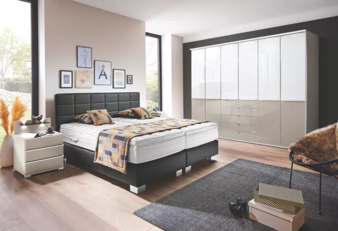 Schlafzimmer mit Boxspringbett und Kleiderschrank aus weißem und kieselgrauen Glas