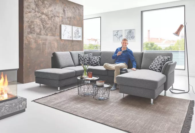 Mann sitzt auf grauer Couch in U-Form